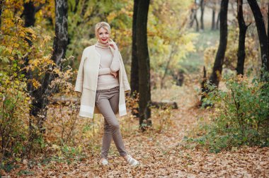 Güzel sarışın kadın sonbahar parkında vakit geçiriyor.