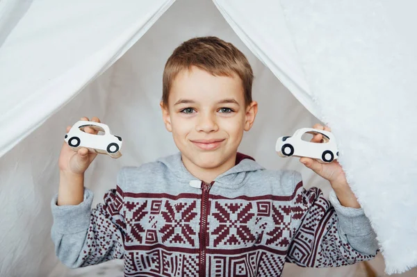 Усміхнена дитина в піжамі тримає дві дерев'яні автомобільні іграшки — стокове фото