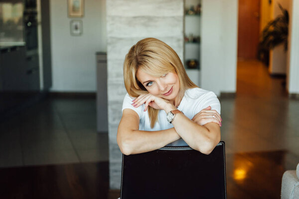 Молодая женщина дома сидит на современном стуле рядом с окном отдыха в гостиной