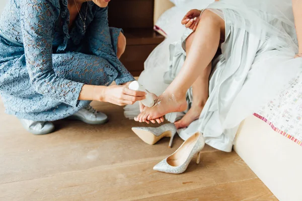 Preparativos de boda. Dama de honor aplica polvo a la pierna de las novias para usar zapatos nupciales cómodamente —  Fotos de Stock