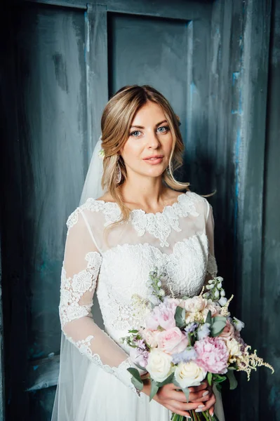 Belle mariée en robe de mariée blanche avec un bouquet de mariage debout près de la porte en bois — Photo