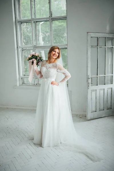 Belle mariée en robe de mariée blanche avec un bouquet de mariage debout près de la porte en bois — Photo