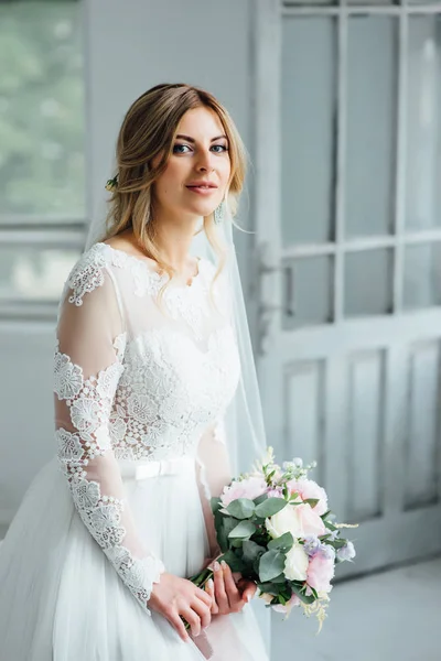 Belle mariée en robe de mariée blanche avec un bouquet de mariage debout près de la porte en bois — Photo