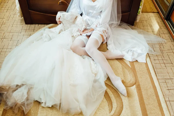Όμορφη νύφη σε λευκά εσώρουχα κάθεται στο κρεβάτι στην κρεβατοκάμαρά της και θέτοντας σε κάλτσες — Φωτογραφία Αρχείου