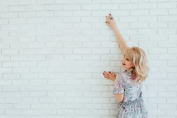 Bionda donna felice in abito leggero con soggiorno di fronte alla parete leggera — Foto Stock