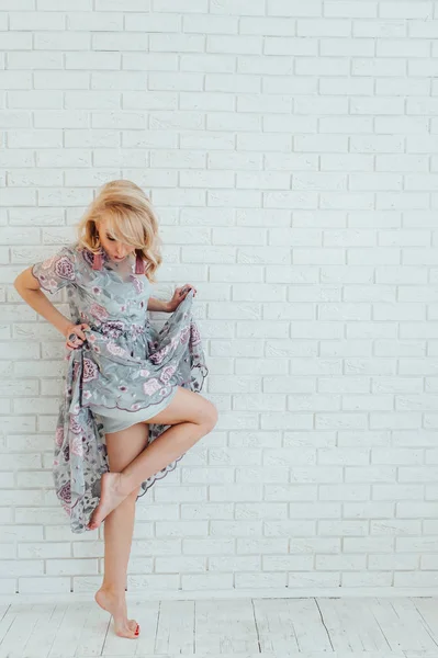Блондинка счастливая женщина в легком платье с пребыванием перед светлой стеной — стоковое фото