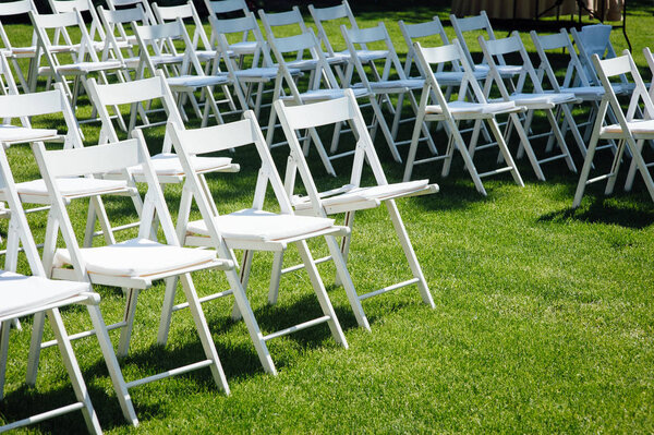 Rows of white folding chairs on lawn before a wedding ceremony in summer