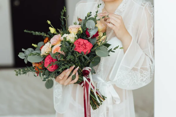 Novia en un vestido blanco sosteniendo un ramo de flores y vegetación — Foto de Stock