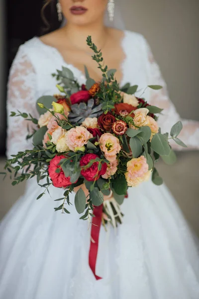 Mariée dans une robe blanche tenant un bouquet de fleurs et de verdure — Photo