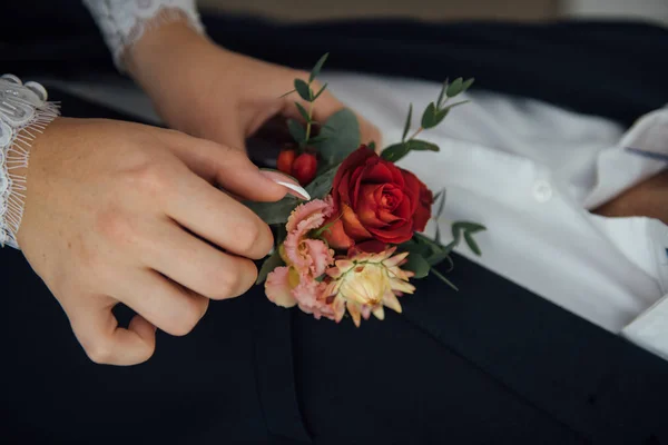 Hands of bride outdoors. Bride corrects boutonniere on grooms wedding jacket — Stock Photo, Image