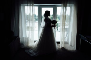 Çekici gelin pencerenin önünde duruyor. Kız odasının penceresinin yanında duruyor. Siluet