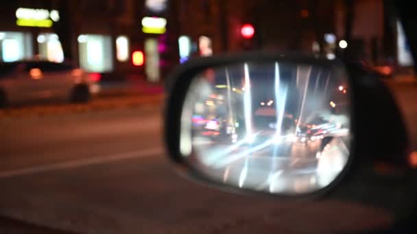 Éjszaka vezetek. A kilátás a kocsiból az oldalsó visszapillantó tükrön. elmosódott városi fények. 4k — Stock videók