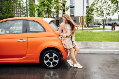 Gorgeous girl with long hair sitting in a red electric car