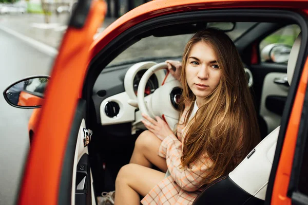 Красивая девушка с длинными волосами сидит в красном электрическом автомобиле — стоковое фото