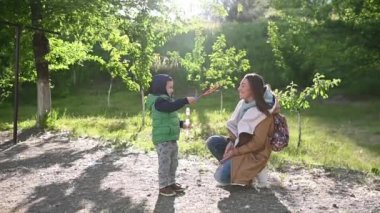 Gülümseyen anne ve küçük oğlu yaz parkında sabun üflüyorlar.