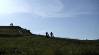İki turist bisikletle yokuş yukarı gider, rahatlar ve mesafeyi izlerler..