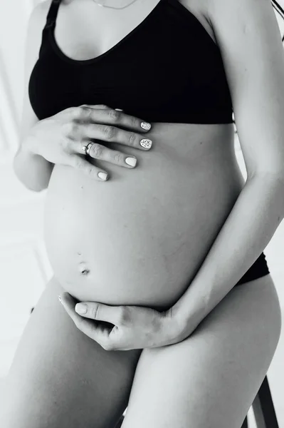Беременная девушка с идеальной фигурой сидит на стуле и держит живот руками — стоковое фото