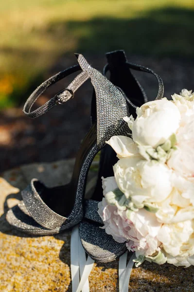 Bruiloft boeket pioenen naast vrouwen schoenen op een steen — Stockfoto