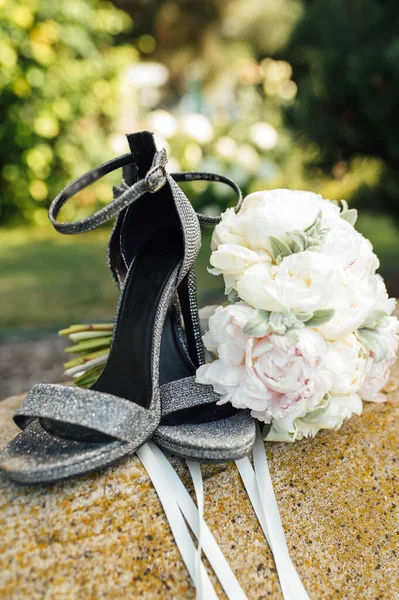 Esküvői csokor bazsarózsa mellett női cipő egy kövön — Stock Fotó