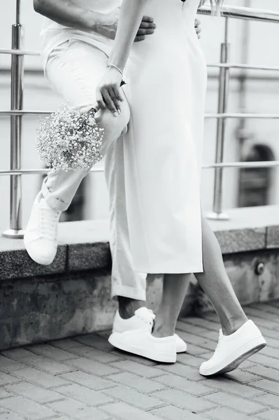 Um casal amoroso em roupas brancas e tênis abraços com as mãos — Fotografia de Stock