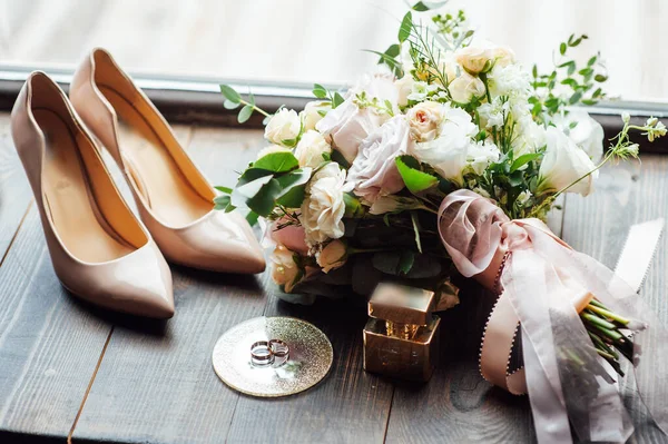 Mooie gouden trouwringen op houten vloer naast boeket en schoenen — Stockfoto