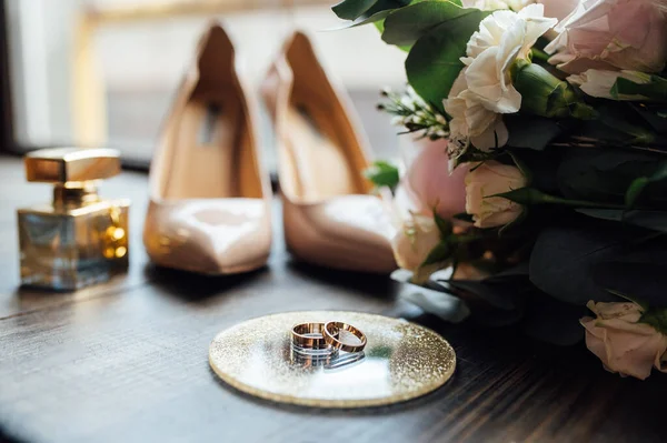 Krásné zlaté snubní prsteny na dřevěné podlaze vedle kytice a boty — Stock fotografie