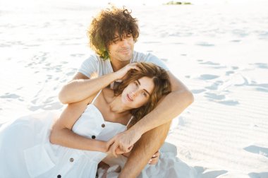 Kıvırcık saçlı bir adam ve güzel bir kız sahilde eğleniyorlar.