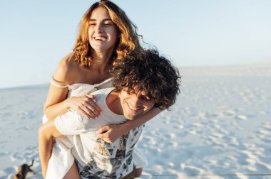 Güzel bir çift sahilde eğleniyor. Neşeli kız sevgililerinin üzerine atladı.