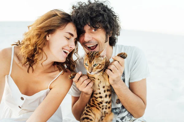 Um homem bonito com cabelo encaracolado abraça suavemente o seu amado. Eles têm um gato nas mãos. — Fotografia de Stock