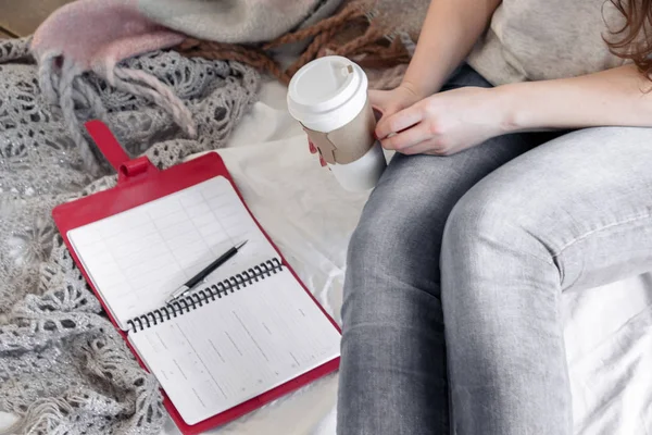 An older woman writes a day plan on a calendar. Next to it is a cup of tea. Business concept. Close up.