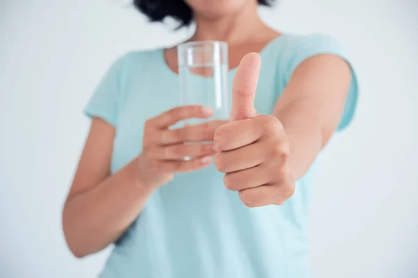 Feliz bela jovem bebendo água. Modelo feminino caucasiano sorridente segurando vidro transparente na mão. Fecha a porta. Foco no braço . — Fotografia de Stock