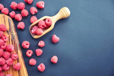 Siyah arka plan üzerine taze organik ahududu. bir tahta kaşık çilek