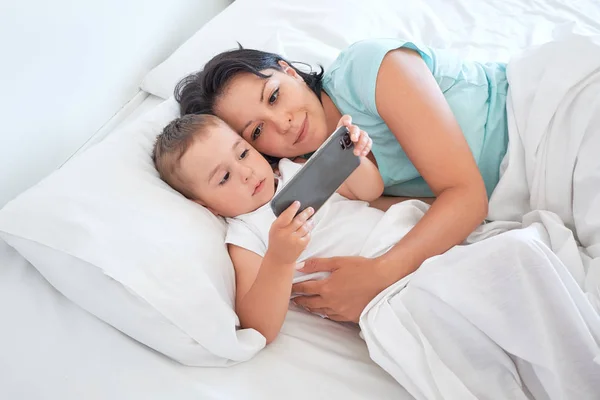 Mom and baby lie together in bed and take selfies — Stock Photo, Image