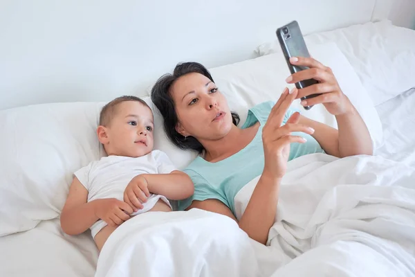 Mama i dziecko leżą razem w łóżku i wziąć autoportrety — Zdjęcie stockowe