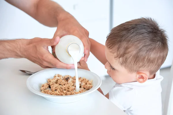 Μικρό αγόρι βοηθά τον μπαμπά να Βάλτε το γάλα στο πλιγούρι βρώμης. Γρήγορο πρωινό στο σπίτι — Φωτογραφία Αρχείου