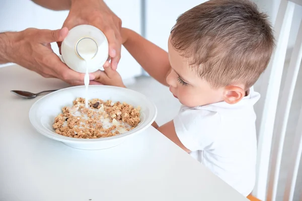 little boy helps dad pour milk into oatmeal. Quick Breakfast at home