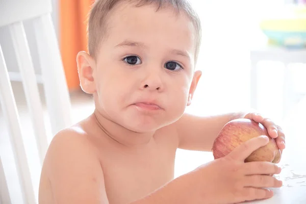 Αστείος αγόρι τρώει ένα μήλο στην κουζίνα. — Φωτογραφία Αρχείου
