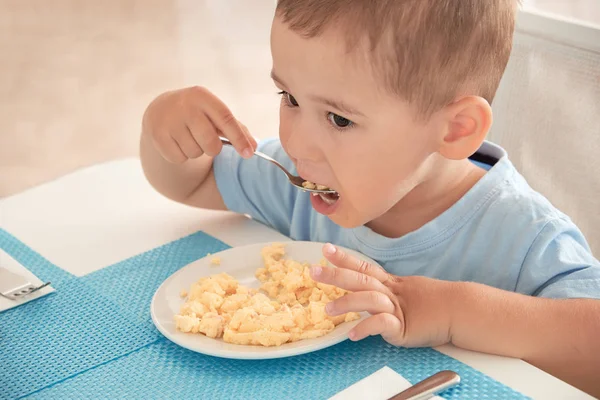 Menino engraçado tem ovos de café da manhã sozinho segurando uma colher — Fotografia de Stock