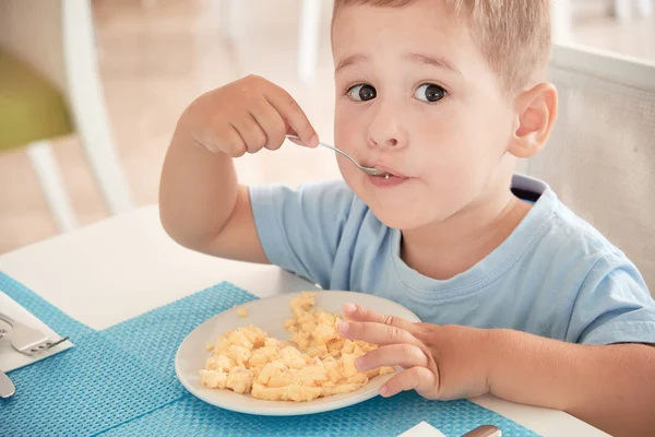 Menino engraçado tem ovos de café da manhã sozinho segurando uma colher — Fotografia de Stock