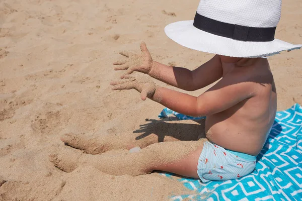 Estilo de vida das crianças ao ar livre. Menino bonito feliz no panamá brincando com areia na praia do mar. Férias de verão e conceito de viagem familiar. Pequeno bebê sentado na areia perto do mar — Fotografia de Stock