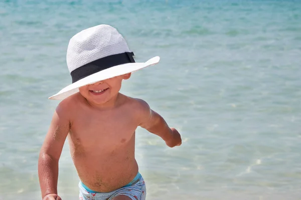 Estilo de vida das crianças ao ar livre. Menino bonito feliz no panamá brincando com areia na praia do mar. Férias de verão e conceito de viagem familiar. Pequeno bebê sentado na areia perto do mar — Fotografia de Stock