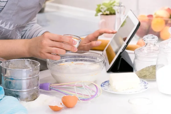 Closeup hands lady standing in kitchen and cooking the dough. Looking at tablet computer. Female following recipe on digital cooking healthy meal. Retro look.