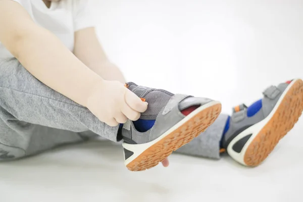 Litet barn försöker sätta på skorna. Baby pojke med skorna i handen. Hur att välja skor för ett barn två år gammal. problemet med platta fötter. — Stockfoto