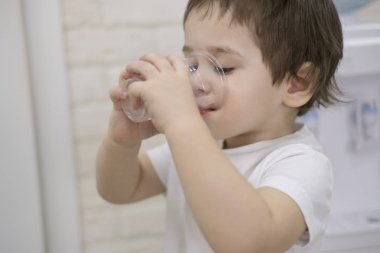 Yakışıklı ciddi tatlı küçük çocuk çocuk kumral ela ile tablo içme suyu tarafından tutarak küçük cam görünümlü dış oturma gözleri üzerinde bulanıklık gri arka plan closeup, yatay kapalı eller