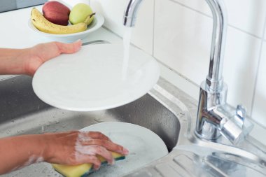 Çekici bir genç kadının kırpılmış görüntüsü evde temizlik yaparken bulaşıkları yıkıyor..