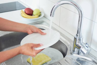 Çekici bir genç kadının kırpılmış görüntüsü evde temizlik yaparken bulaşıkları yıkıyor..