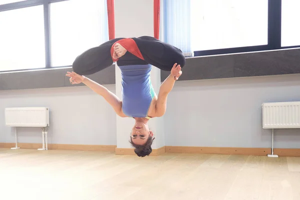 Adult woman practices aero anti-gravity yoga position in studio. Inversion bow pose in aero anti gravity yoga. Aerial exercises