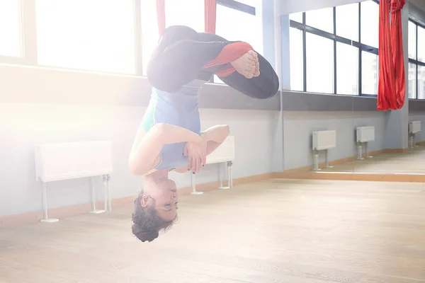Adult woman practices aero anti-gravity yoga position in studio. Inversion bow pose in aero anti gravity yoga. Aerial exercises