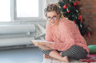 kıvrımlı genç kız Noel sabahı bir kitap okur. afrika pigtails kız modeli artı boyutu ile sarışın
