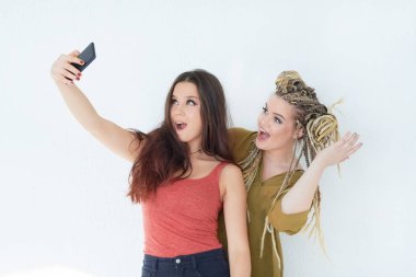 iki arkadaş beyaz bir duvarın arka planında selfie çekmek. ergenlerin sosyal ağlara bağımlılığı. Genç mutlu kızlar birlikte eğlenin.